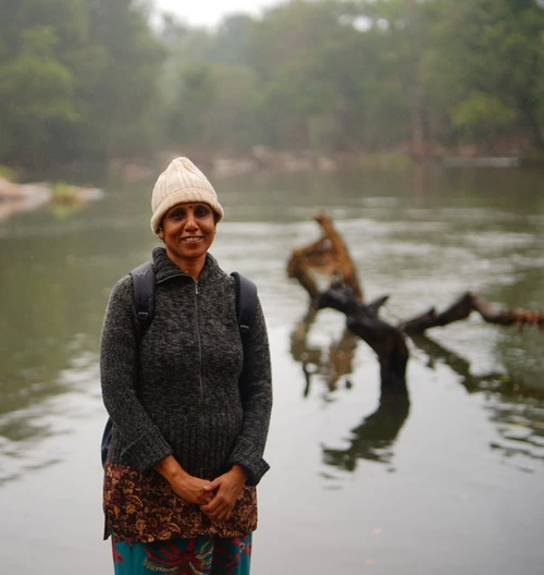Woman trekker standing near a calm jungle river with forest trees and natural scenery in the background